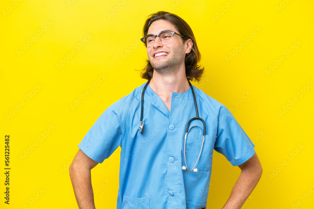 Young surgeon caucasian man isolated on yellow background posing with arms at hip and smiling Young surgeon caucasian man isolated on yellow background posing with arms at hip and smiling