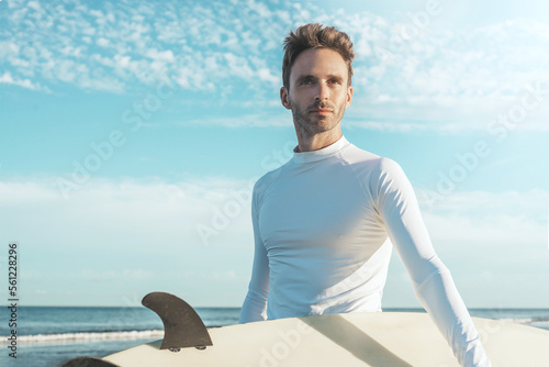 Photos Young handsome surfer guy wearing an empty blank lycra t-shirt and holding a surfboard