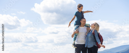 Family standing with arms around on top of mountain, looking at beautiful summer mountain landscape. People enjoying view.