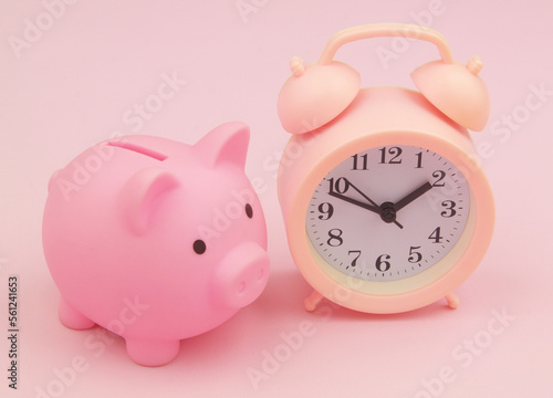 Pink piggy bank with alarm clock on pink background close up. Time for save money concept.
