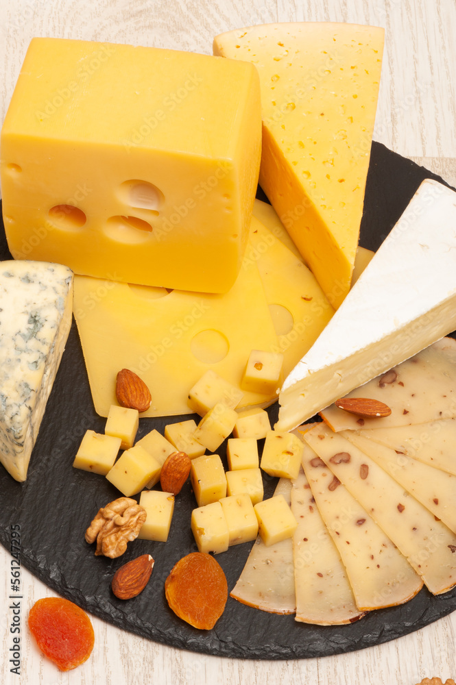 Fototapeta premium Different types of cheese on a black graphite board decorated with dried apricots and nuts
