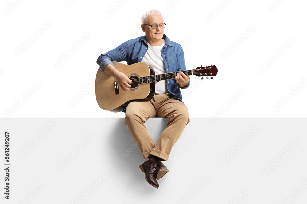 Mature man seated on a blank panel playing an acoustic guitar Mature man seated on a blank panel playing an acoustic guitar