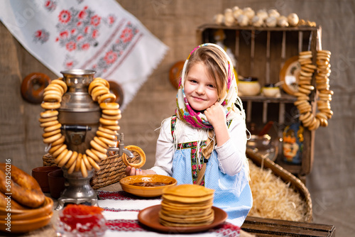 Little girl in folk Russian headscarf and dress with bagels and pancake celebrating Maslenitsa photo