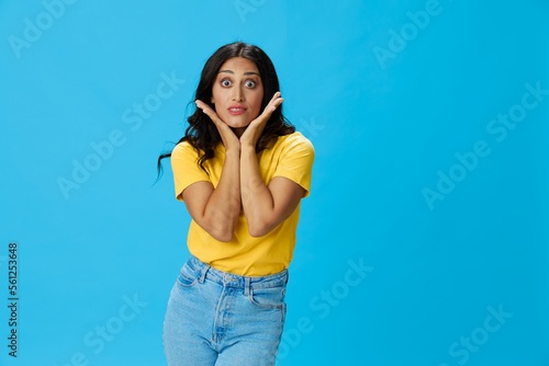 Woman in yellow t-shirt on blue background posing gestures emotions and signals with smile, hands up happiness copy space
