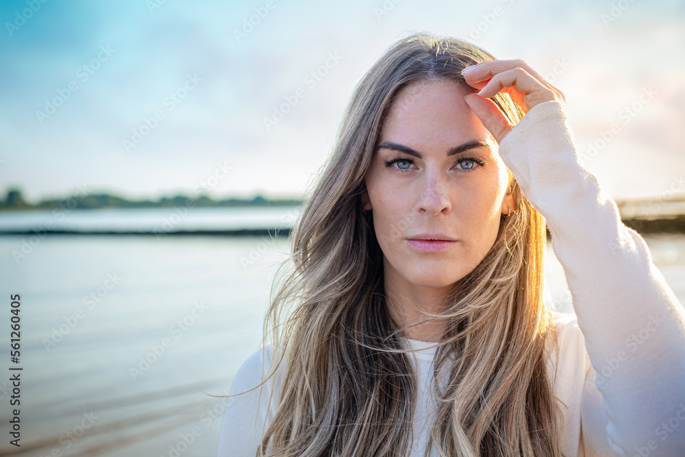 portrait of a beautiful young Women on a beach with sunlight and water in background looking confident into camera