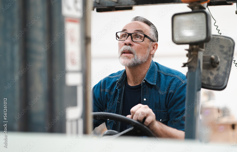 Male factory manager working in warehouse driving forklift truck. Portrait of forklift driver employee transporting merchandise in storehouse delivering to shelf. Industrial worker in industry vehicle Male factory manager working in warehouse driving forklift truck. Portrait of forklift driver employee transporting merchandise in storehouse delivering to shelf. Industrial worker in industry vehicle