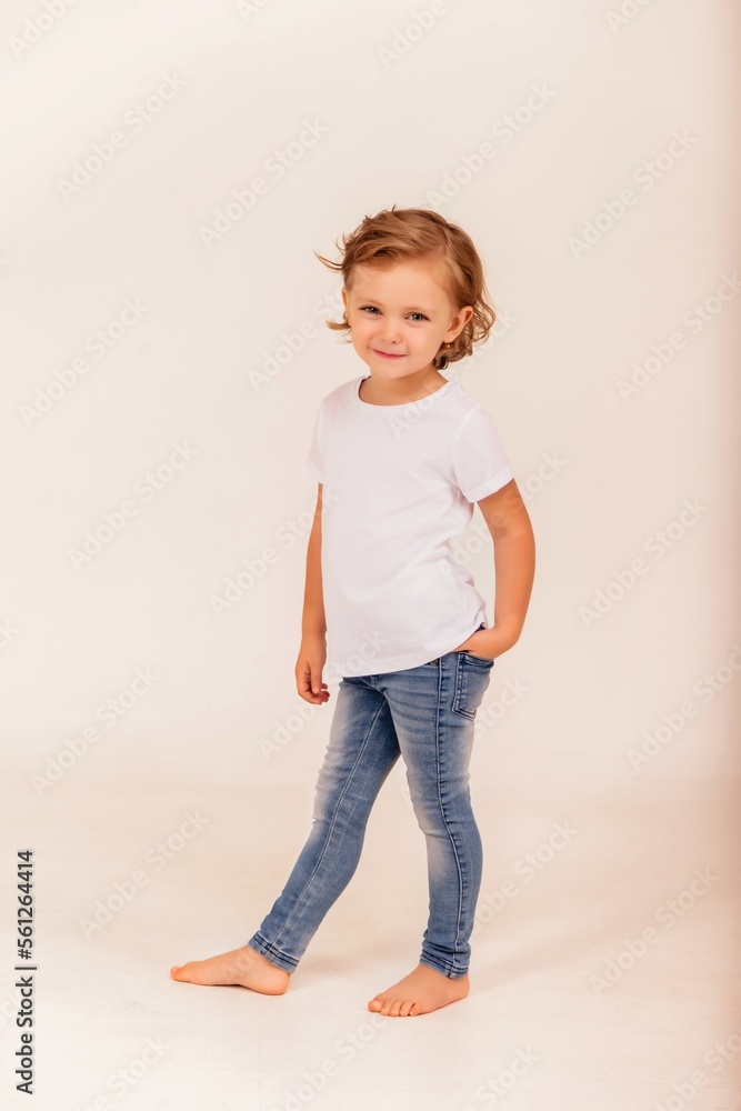 Full length trendy funny little girl model posing in jeans and t-shirt on white background, looking at camera. Studio shot youth style child. Fashion style concept. Copy text space for advertising