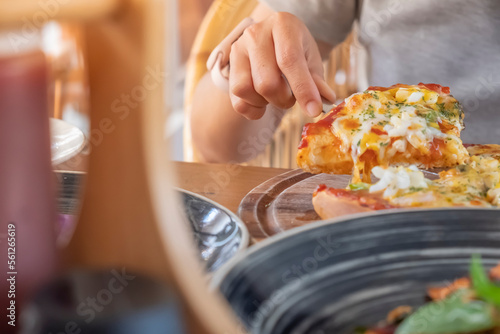 Closeup of a woman's hand scooping homemade pizza on a wooden plate to share on a plate with cheese stretched out, colorful toppings look appetizing