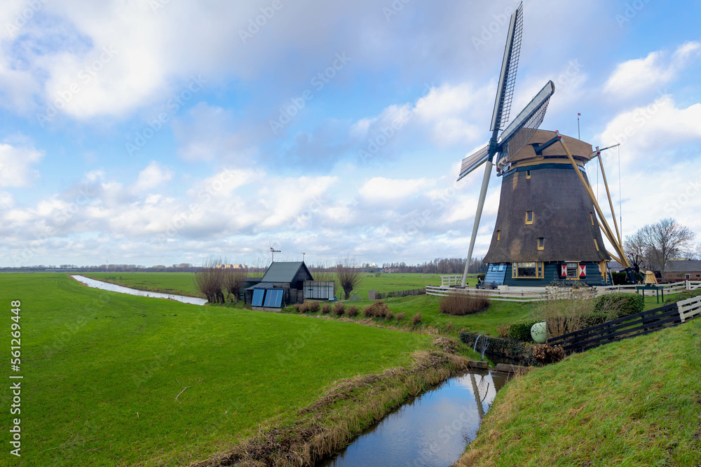 Countryside landscape view of traditional Dutch windmill under blue sky in winter, Polder, water and low land, Small canal, ditch with green grass field along Gein river, Abcoude, Utrecht Netherlands.