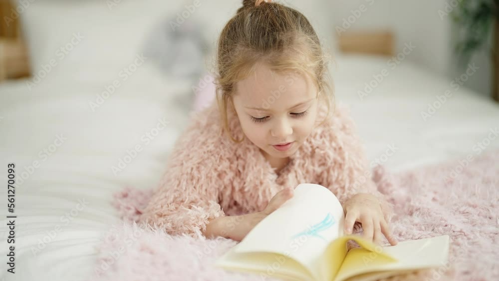Adorable blonde girl reading book lying on bed at bedroom Adorable blonde girl reading book lying on bed at bedroom
