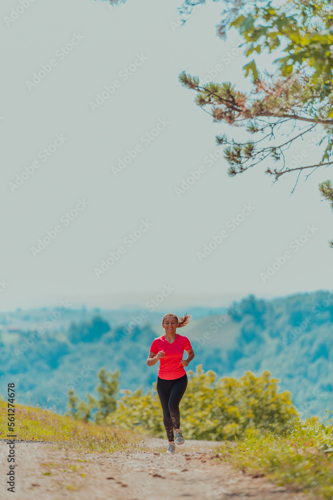 Young happy woman enjoying in a healthy lifestyle while jogging on a country road through the beautiful sunny forest, exercise and fitness concept