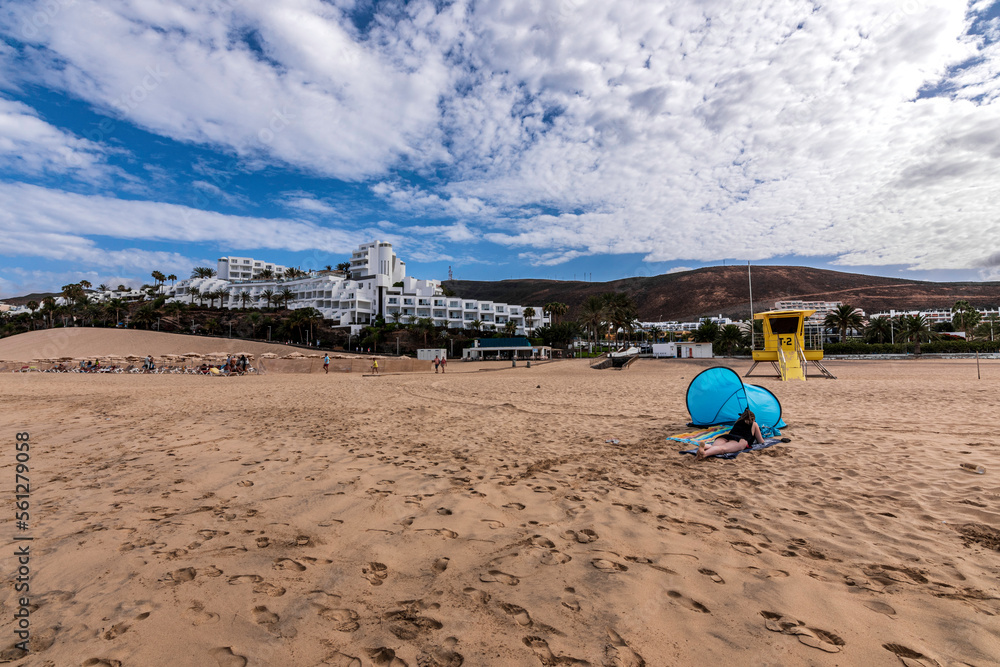 Pajara beach with the view of a girl lying on the golden sand near her tent. In the background of Jandia beach you can see the buildings of Morro Jable. Sunny day with some clouds. Pajara beach with the view of a girl lying on the golden sand near her tent. In the background of Jandia beach you can see the buildings of Morro Jable. Sunny day with some clouds.