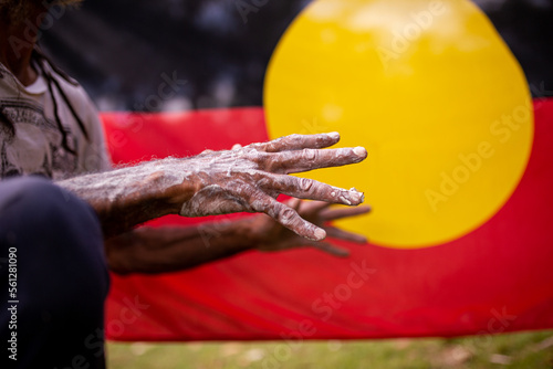 Hands covered in white paint in front of the Aboriginal Flag