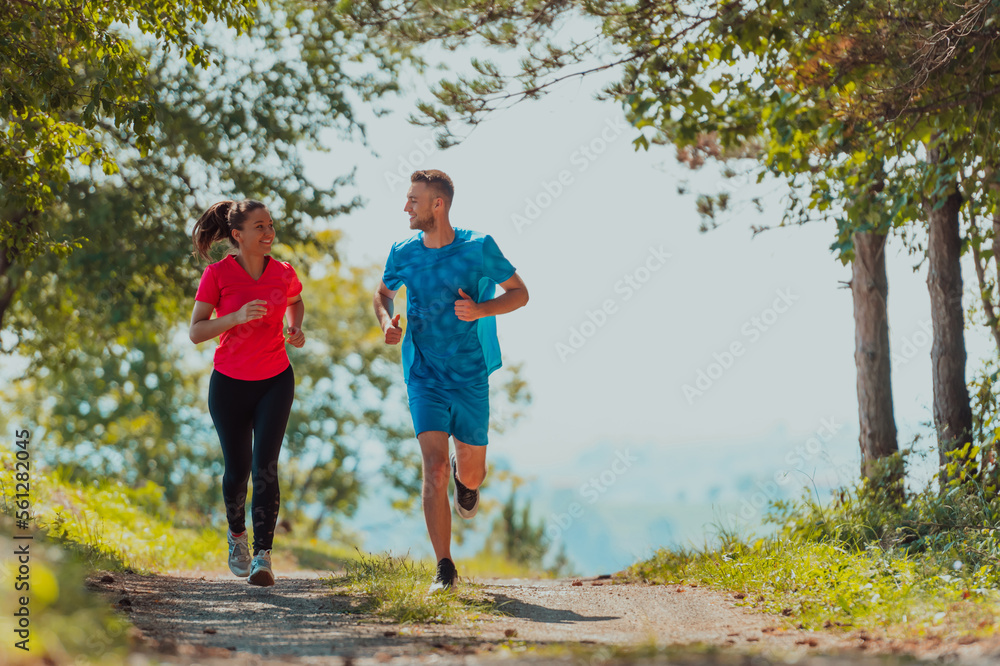 Couple enjoying in a healthy lifestyle while jogging on a country road through the beautiful sunny forest, exercise and fitness concept Couple enjoying in a healthy lifestyle while jogging on a country road through the beautiful sunny forest, exercise and fitness concept