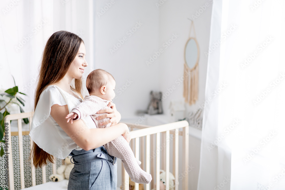 mom holds a small newborn baby girl in her arms at home in a