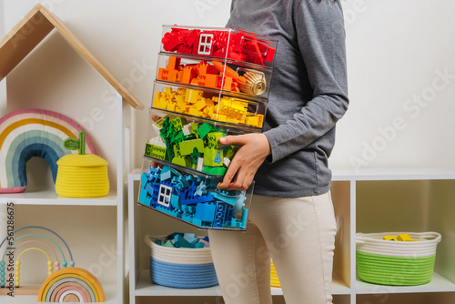 Young woman is holding storage boxes toys. Mom sorted by colors children's toys in transparent plastic boxes. Mother tidy up the children's room. Organization and Storage Ideas in playroom. photo
