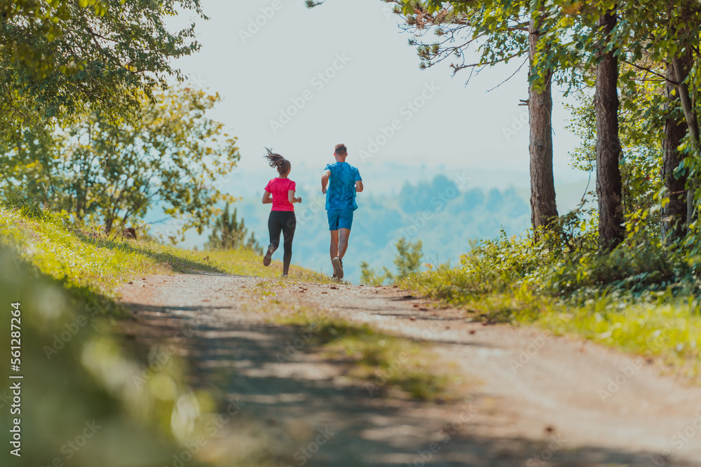 Couple enjoying in a healthy lifestyle while jogging on a country road through the beautiful sunny forest, exercise and fitness concept