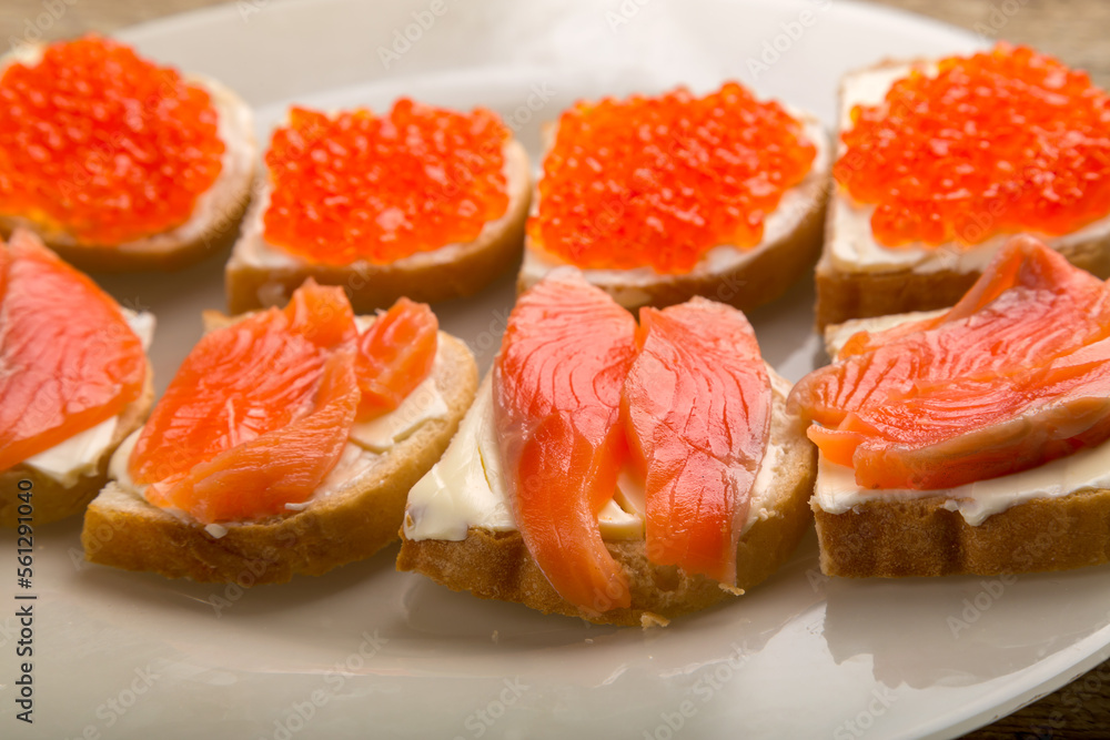 Toasts with red caviar and salted trout and butter on a plate close-up.