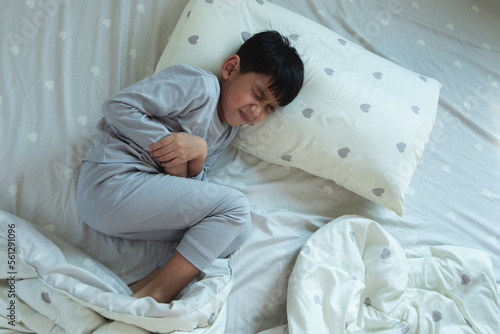 Top View of Asian boy lying in bed with stomach ache