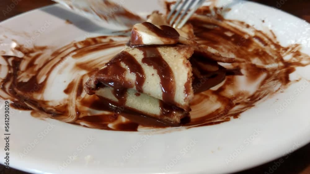 The girl cuts a sweet pancake with chocolate and banana with a knife. The girl cuts a sweet pancake with chocolate and banana with a knife.