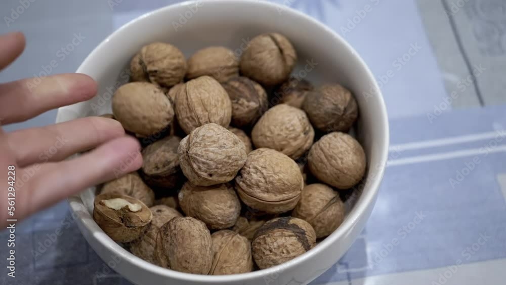 Farmer Hands Putting Walnuts in a Bowl with Collected Nuts on the Table. Close-up. Autumn harvest of ripe, fresh walnuts. Useful healthy food. Brain food. Diet food. Vegetarianism. Walnut shell. Farmer Hands Putting Walnuts in a Bowl with Collected Nuts on the Table. Close-up. Autumn harvest of ripe, fresh walnuts. Useful healthy food. Brain food. Diet food. Vegetarianism. Walnut shell.