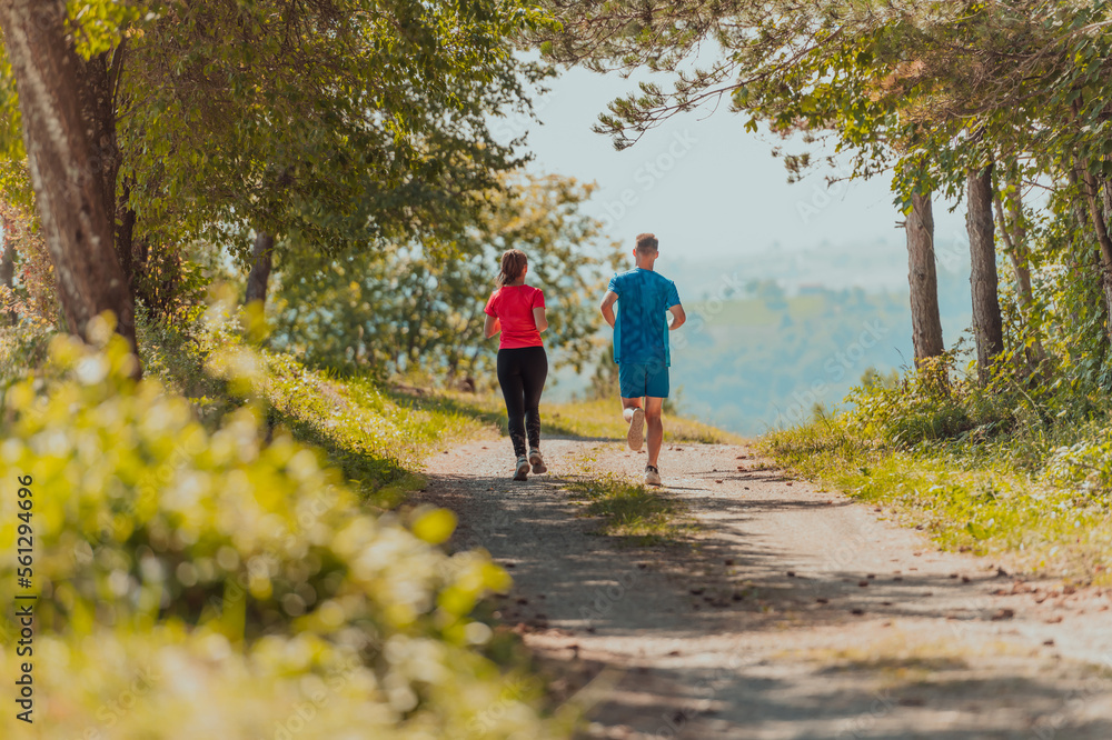 Fototapeta premium Couple enjoying in a healthy lifestyle while jogging on a country road through the beautiful sunny forest, exercise and fitness concept