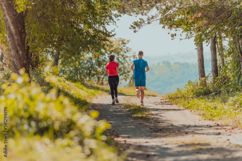 Couple enjoying in a healthy lifestyle while jogging on a country road through the beautiful sunny forest, exercise and fitness concept