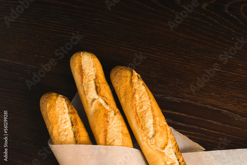 Delicious baguettes from the bakery close-up, wrapped in baking paper, on a dark wooden background with copy space