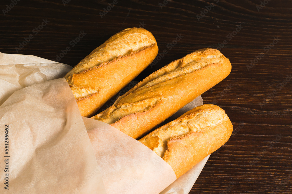 Delicious baguettes from the bakery wrapped in baking paper, on a dark wooden background