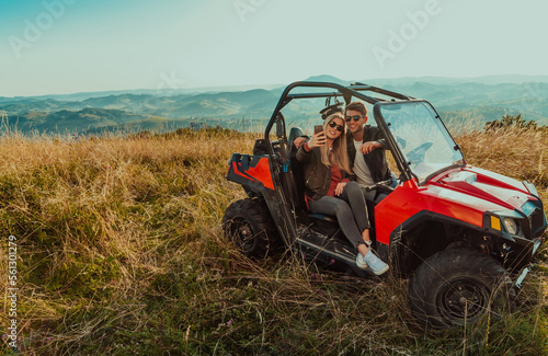 Young happy excited couple enjoying beautiful sunny day taking selfie picture while driving a off road buggy car on mountain nature