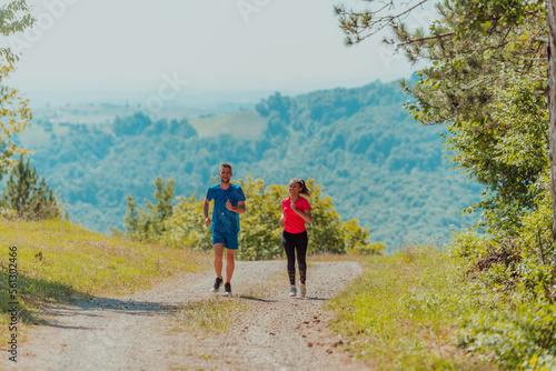 Couple enjoying in a healthy lifestyle while jogging on a country road through the beautiful sunny forest  exercise and fitness concept