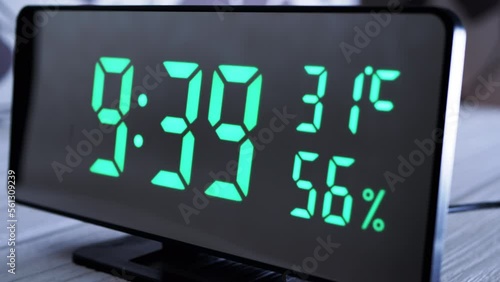 Digital Clock Showing Time on Green Display 9:39 AM, Temperature, Air Humidity. Modern mirror clock, alarm clock with a thermometer, hydrometer standing on a desk on white background. Time concept. photo