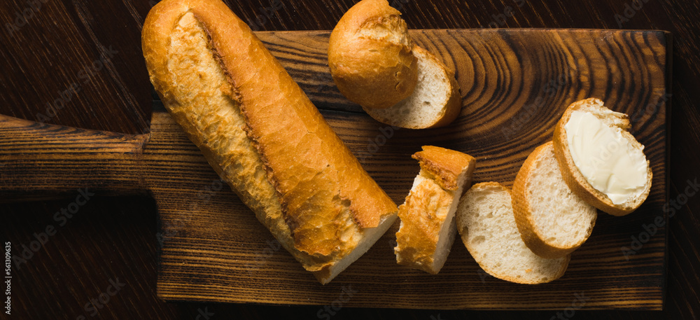 Appetizing baguette with butter on a wooden cutting board, flatlay