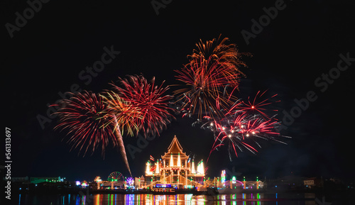 Beautiful fireworks in night sky over Wat Krok Krak Thai temple with decorative lighting and light reflection on river surface in annual festival area at night in Samutsakhon, Thailand