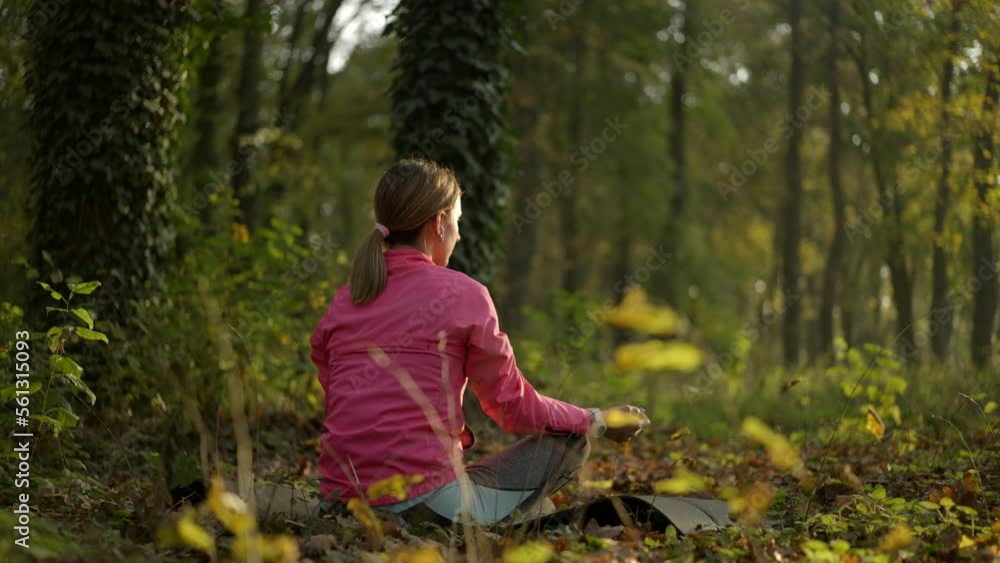 Beautiful sporty woman doing yoga in lotus position and breathing exercise in a serene forest at sunset