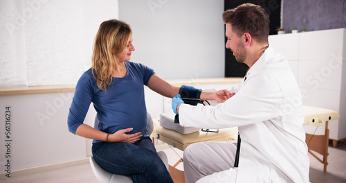 Male Doctor Measuring Blood Pressure Of Pregnant Woman