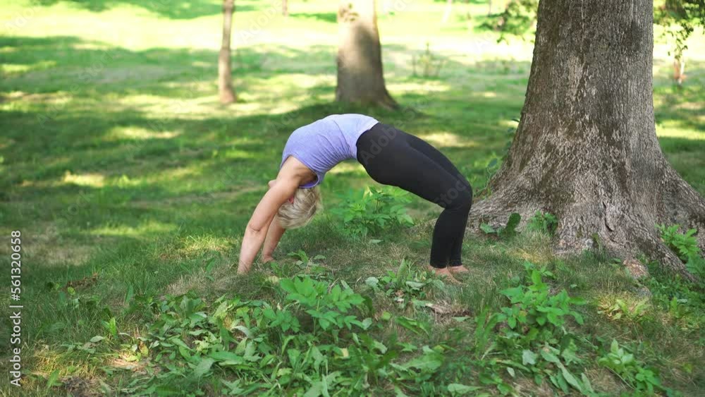 Middle-aged woman doing yoga in sportswear outdoors in a city park in wheel pose.Urdhva Dhanurasana . Full length.The concept of stretching, pilates, healthy lifestyle. Middle-aged woman doing yoga in sportswear outdoors in a city park in wheel pose.Urdhva Dhanurasana . Full length.The concept of stretching, pilates, healthy lifestyle.