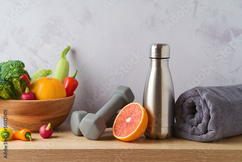 Healthy lifestyle and fitness concept. Bottle of water, dumbbells; towel, fruits and vegetables on wooden table over modern background