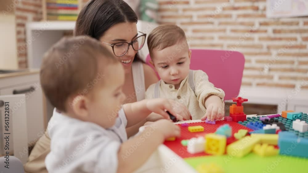 Teacher with boys playing with construction blocks sitting on table at kindergarten Teacher with boys playing with construction blocks sitting on table at kindergarten