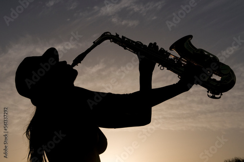 silhouette of young woman playing saxophone at sunset in backlight