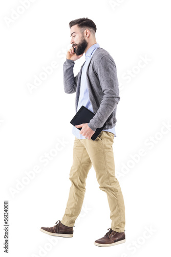 Side view of business man walking, carrying tablet and talking on the cellphone. Full body length portrait isolated on transparent background.