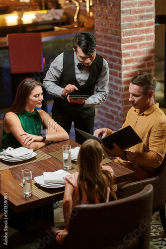 Restaurant waiter taking notes on tablet computer when taking order from family