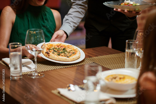 Waiter putting plate with pizza in front of woman