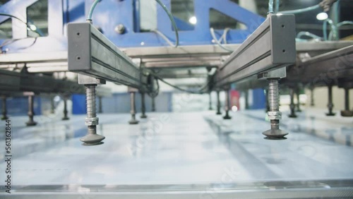Transparent sheet of polycarbonate moves along conveyor belt. Manipulator with vacuum suction cups takes and lifts sheet up at modern factory closeup