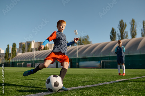 Boy playing football on field and kicking soccer ball