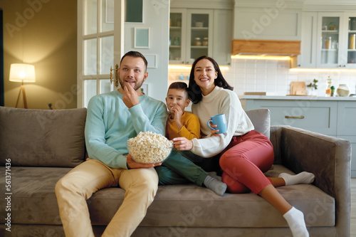 Happy family watching movie eating popcorn sitting on sofa in living room