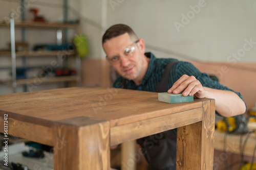 Male carpenter finishing work on wooden table in workshop. 