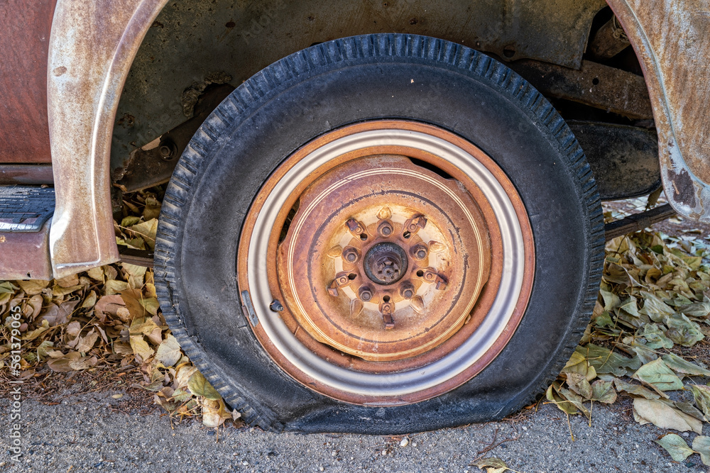 A flat tire on a rusty antique car