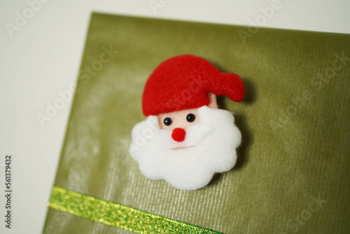 Gift box with green bow and Santa Claus head lying on sofa, close-up 