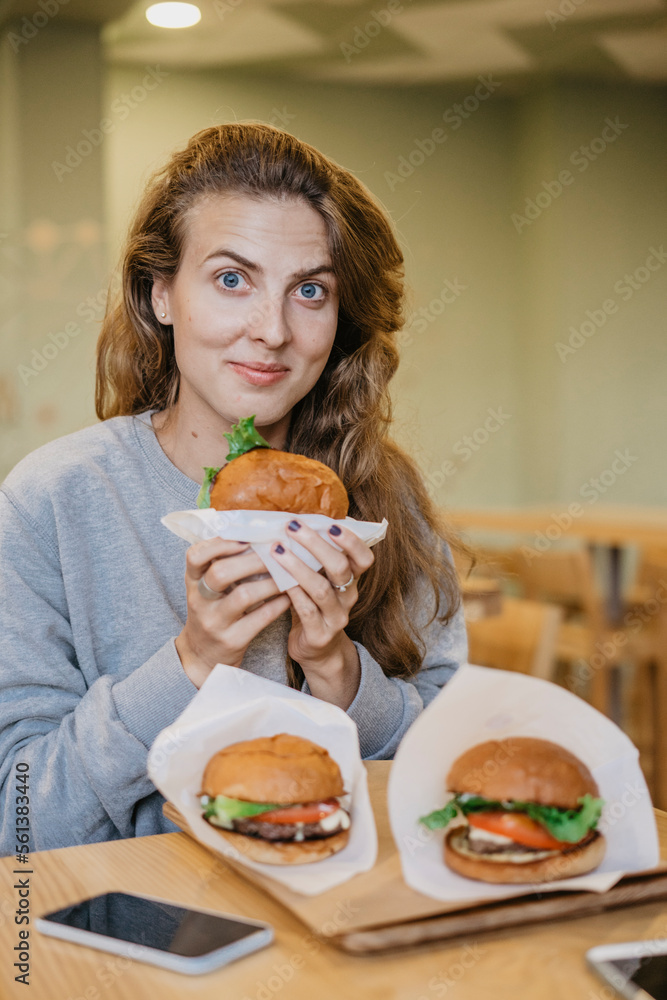 Portrait of woman eating burgers while sitting at table in restaurant Portrait of woman eating burgers while sitting at table in restaurant